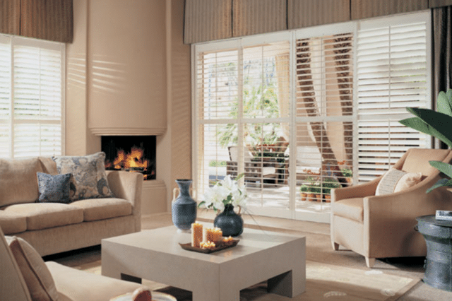 A living room with large windows with plantation shutters with the slats open for sunlight.