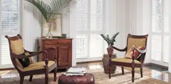 Living room area surrounded by furniture, lamps, and shutters on the large windows.