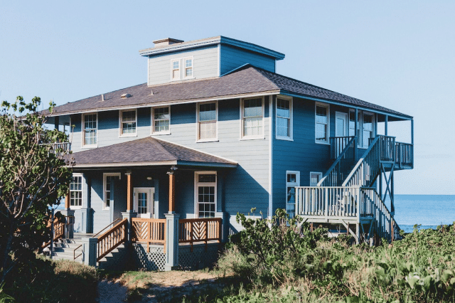 The blue exterior of an oceanfront home is featured, with calm ocean waters in the backdrop.
